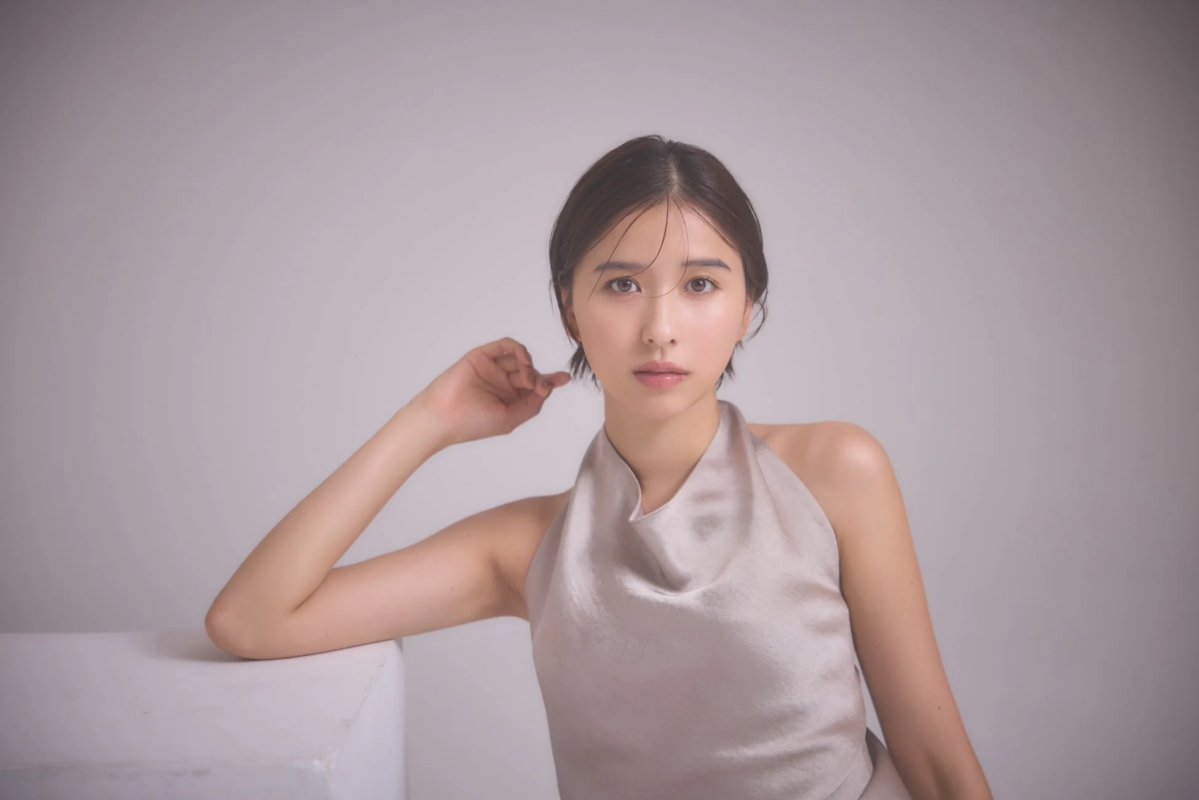 スタジオで撮影された、ショートヘアの若い女性のポートレート。ベージュのホルターネックトップスを着用し、肘をついてカメラを見つめている。落ち着いた雰囲気の美しい写真です。