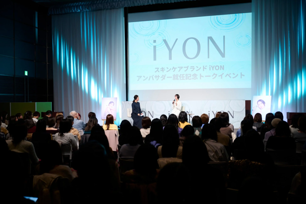 スキンケアブランド「iYON」のアンバサダー就任記念トークイベントが開催され、ステージ上で二人の女性がトークを繰り広げている。会場には多数の観客が集まり、スクリーンにはブランド名が表示されている。