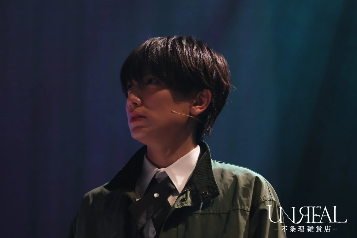 暗い背景のステージで、ピンマイクを付けた若い男性