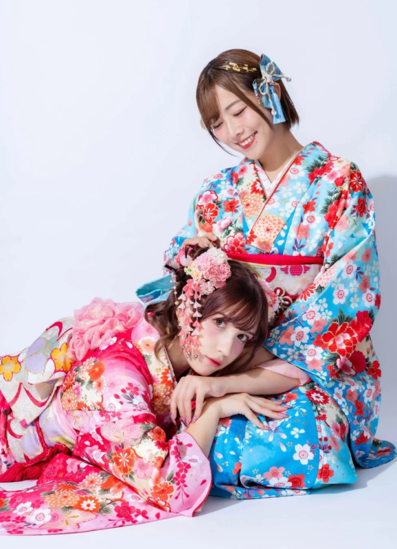 鮮やかな花柄の着物をまとった二人の女性が、笑顔で寄り添い合うポートレート