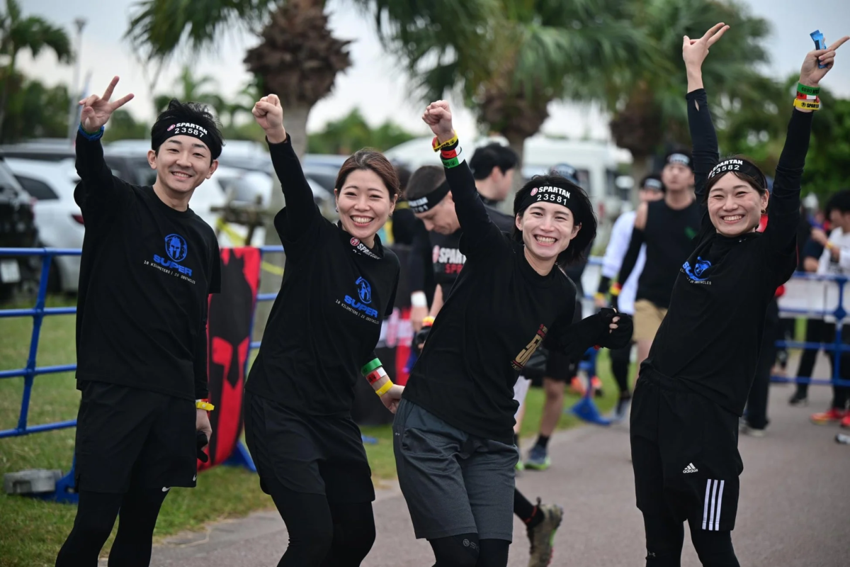 スパルタンレースに参加する4人の男女が、レース中に笑顔でポーズをとっています