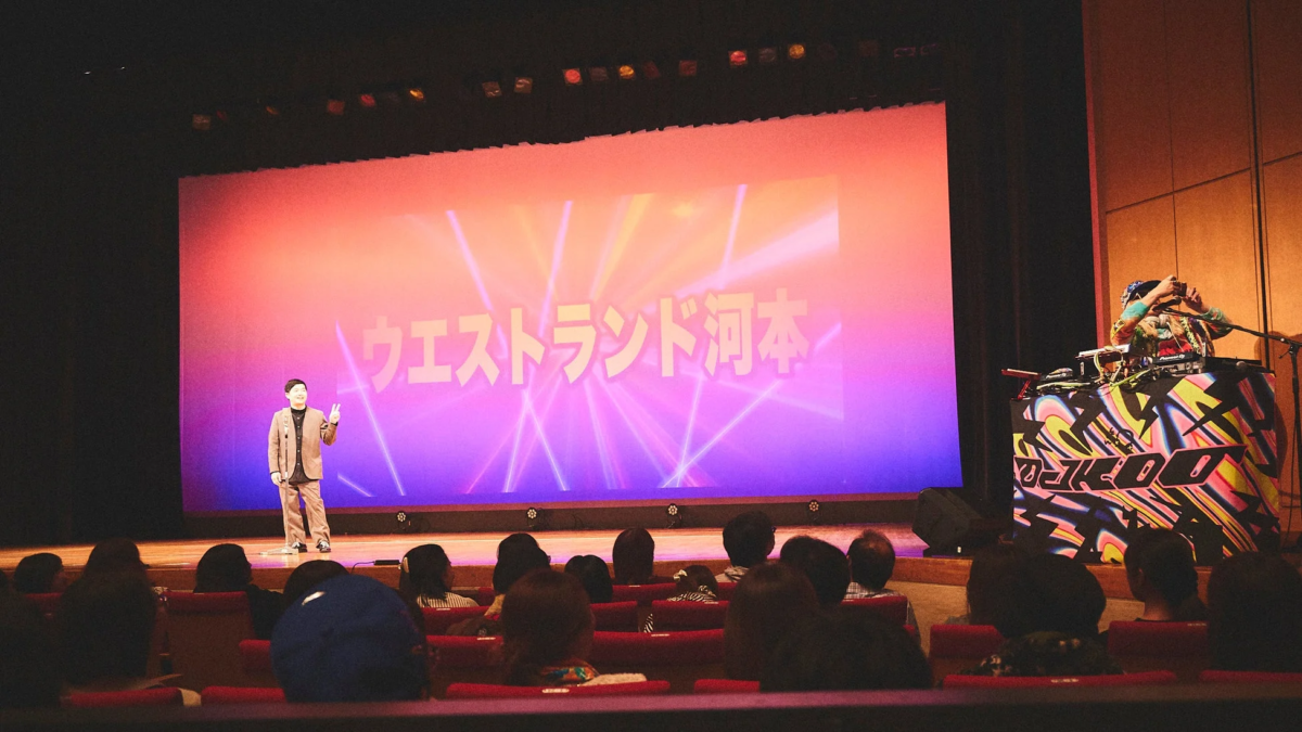 ライブ会場のステージで、男性パフォーマーが観客の前でピースサインをしています