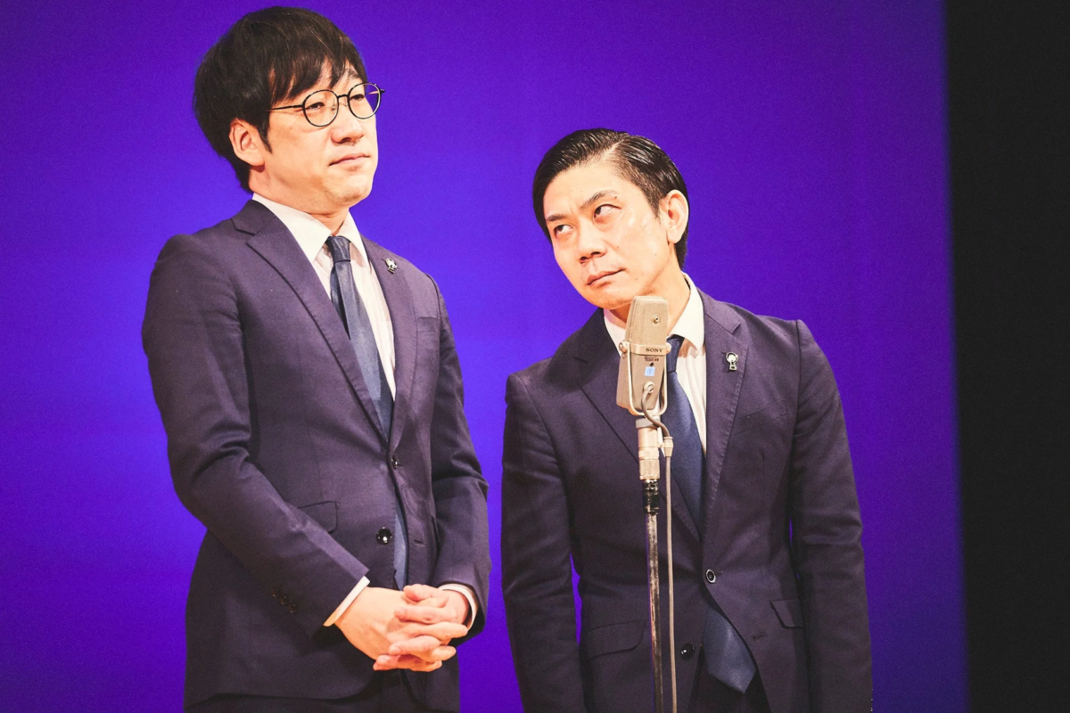 青い背景のステージに立つ2人の日本人男性
