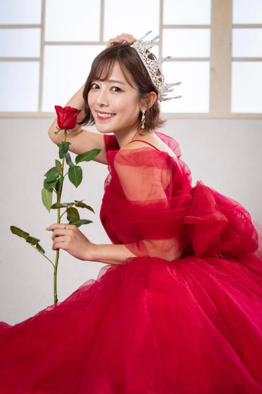 赤いドレスとティアラを身につけ、笑顔で赤いバラを持つ女性