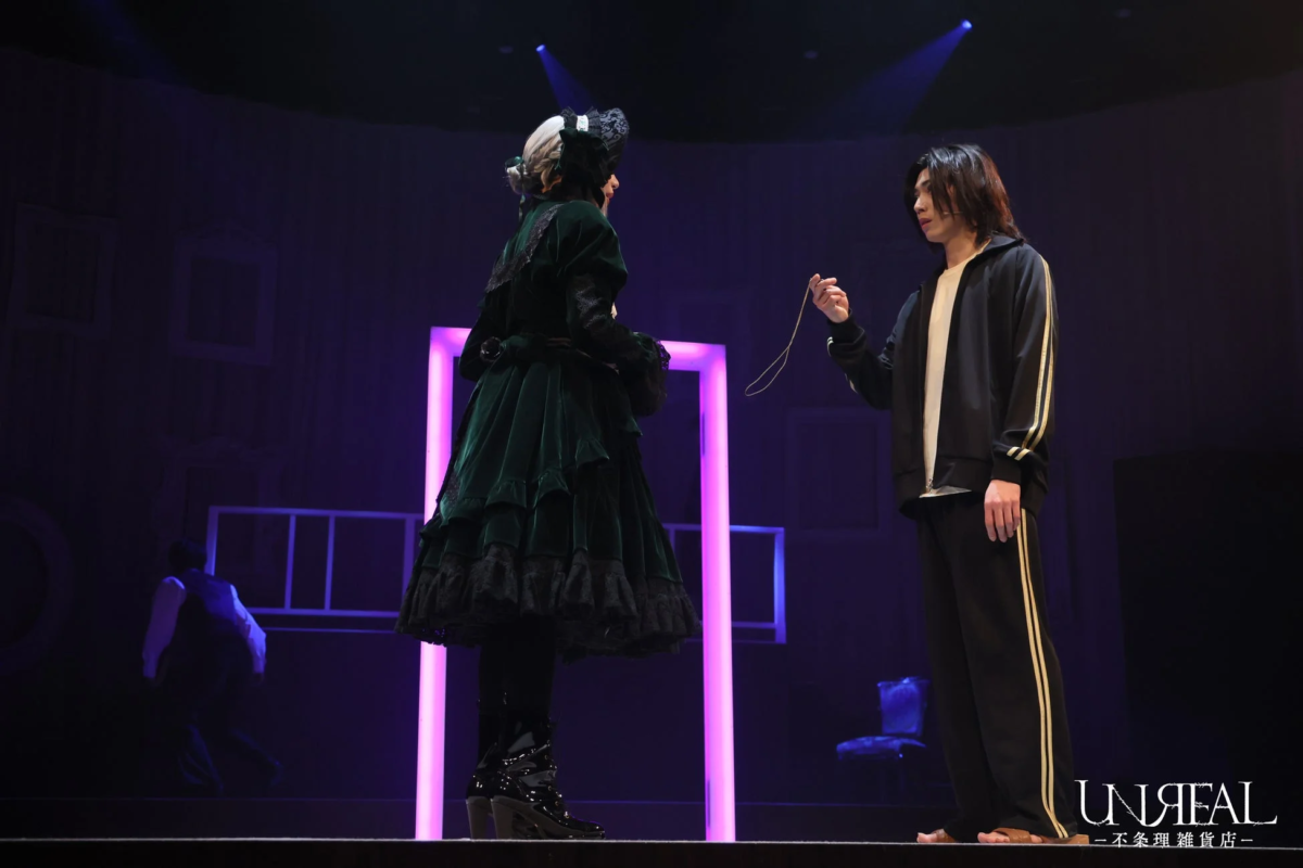 舞台上で、豪華な深緑の衣装と黒いジャージ姿の二人が向かい合う