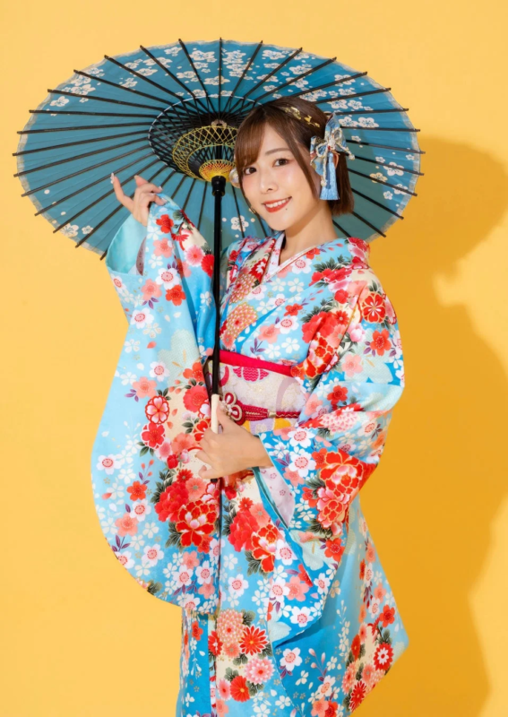 鮮やかな花柄の青い振袖を着た女性が、青い和傘を手に持ち、明るい笑顔を見せている