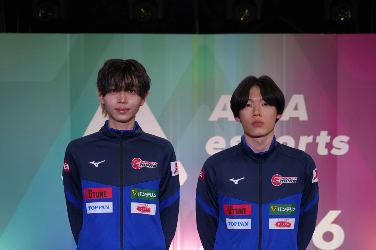 eスポーツジャパンのユニフォームを着た2人の若い日本人男性がステージに立っています。背景にはeスポーツ関連の文字が見え、ユニフォームにはミズノ、GTUNE、TOPPAN、バンテリン、めぐりズムといった複数のスポンサーロゴが配置されています。