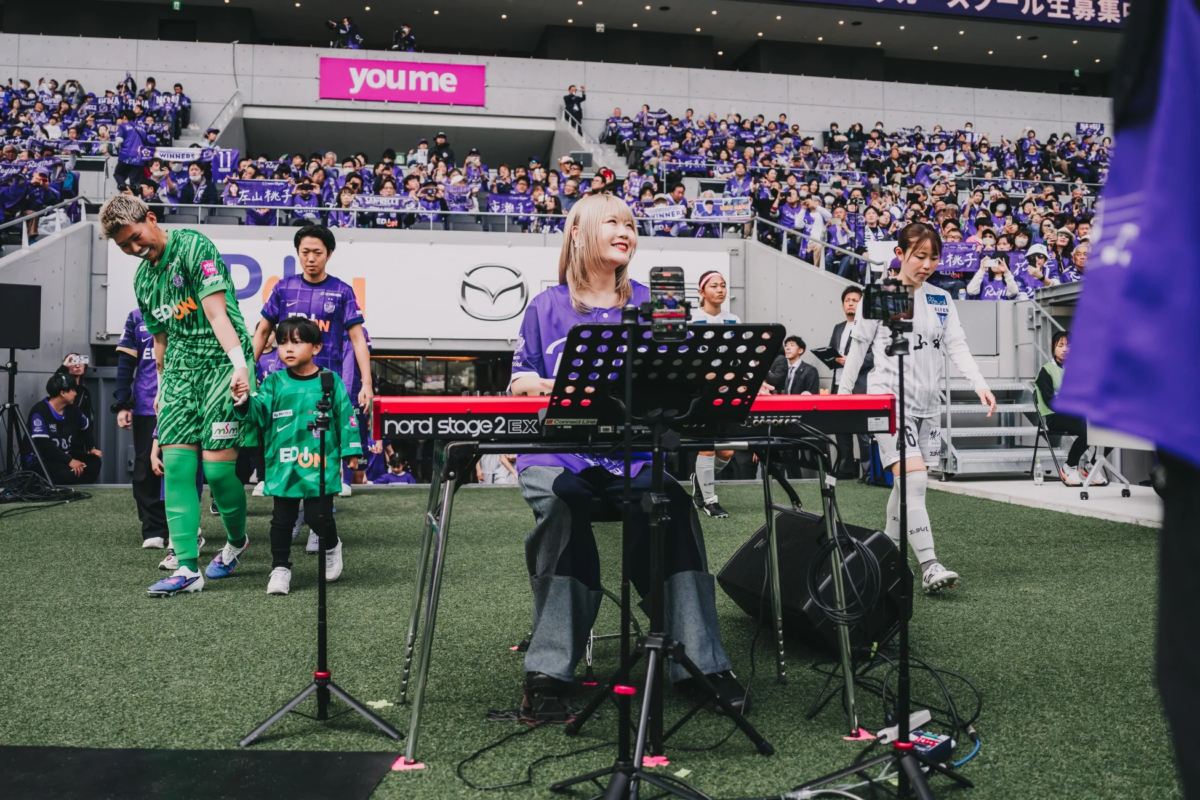 サッカー場のイベントでキーボードを演奏する女性と選手、子供
