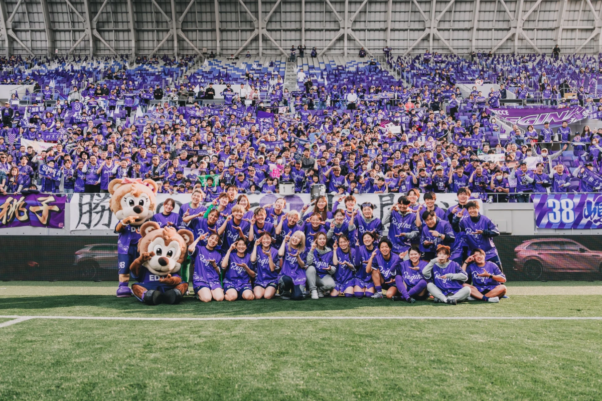 女子サッカーチームの選手とマスコット、サポーターが集合写真