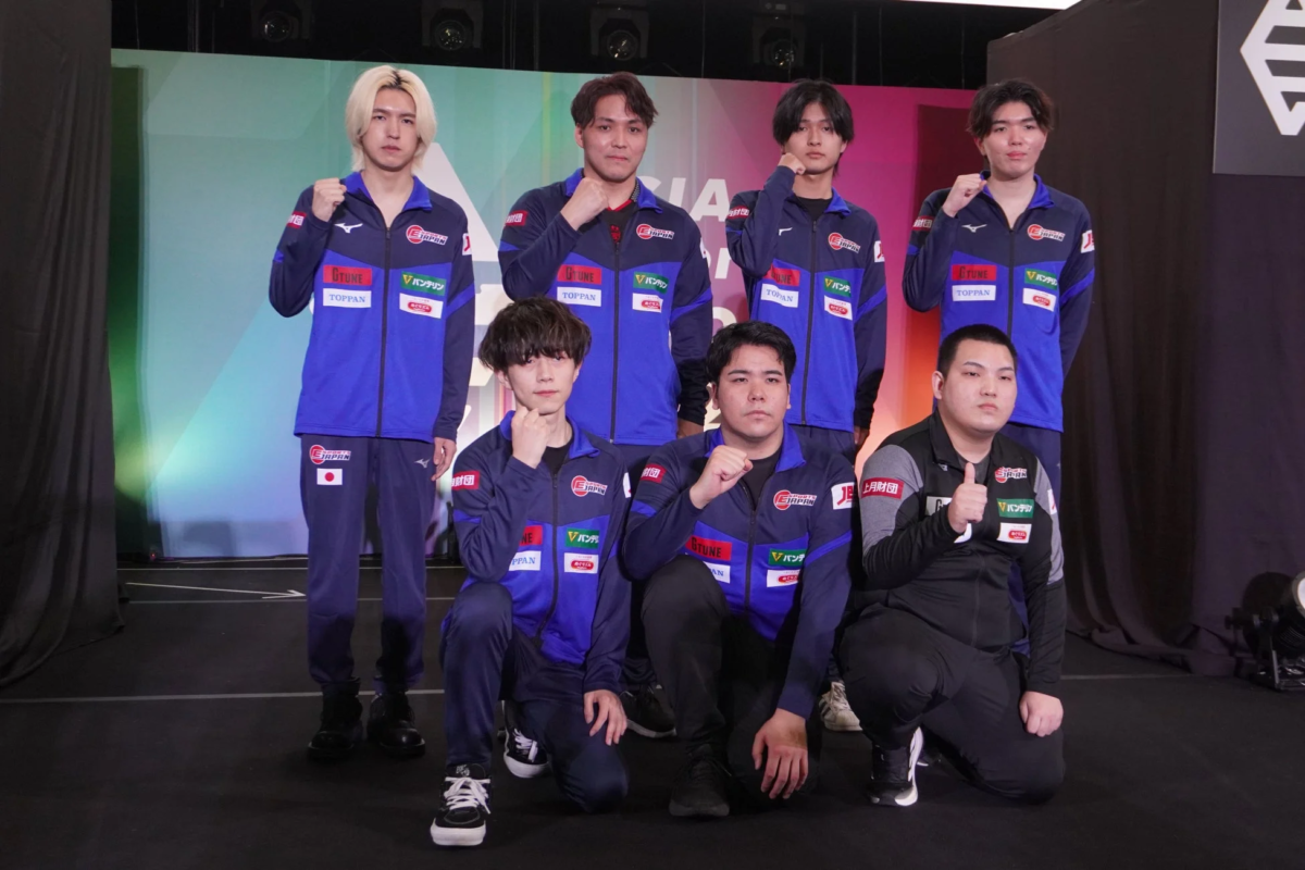 「eJAPAN」のロゴが入ったユニフォームを着用した男性eスポーツ選手たちが、イベント会場のような場所で集合写真を撮っている。皆、拳を握り、意気込みを感じさせるポーズをとっている。