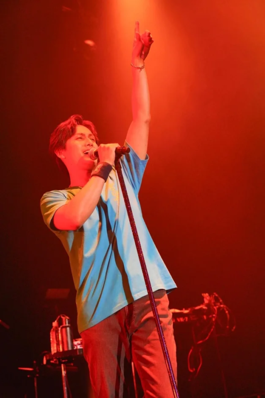 赤い照明のステージでマイクを手に歌う男性