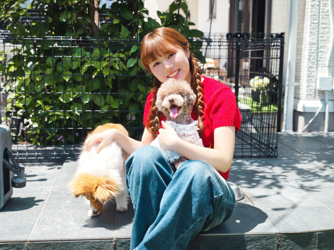 屋外で二匹の愛犬とくつろぐ若い女性。女性は笑顔で、一匹の犬を抱きかかえ、もう一匹は傍らにいます。晴れた日の穏やかなひとときが伝わる一枚です。