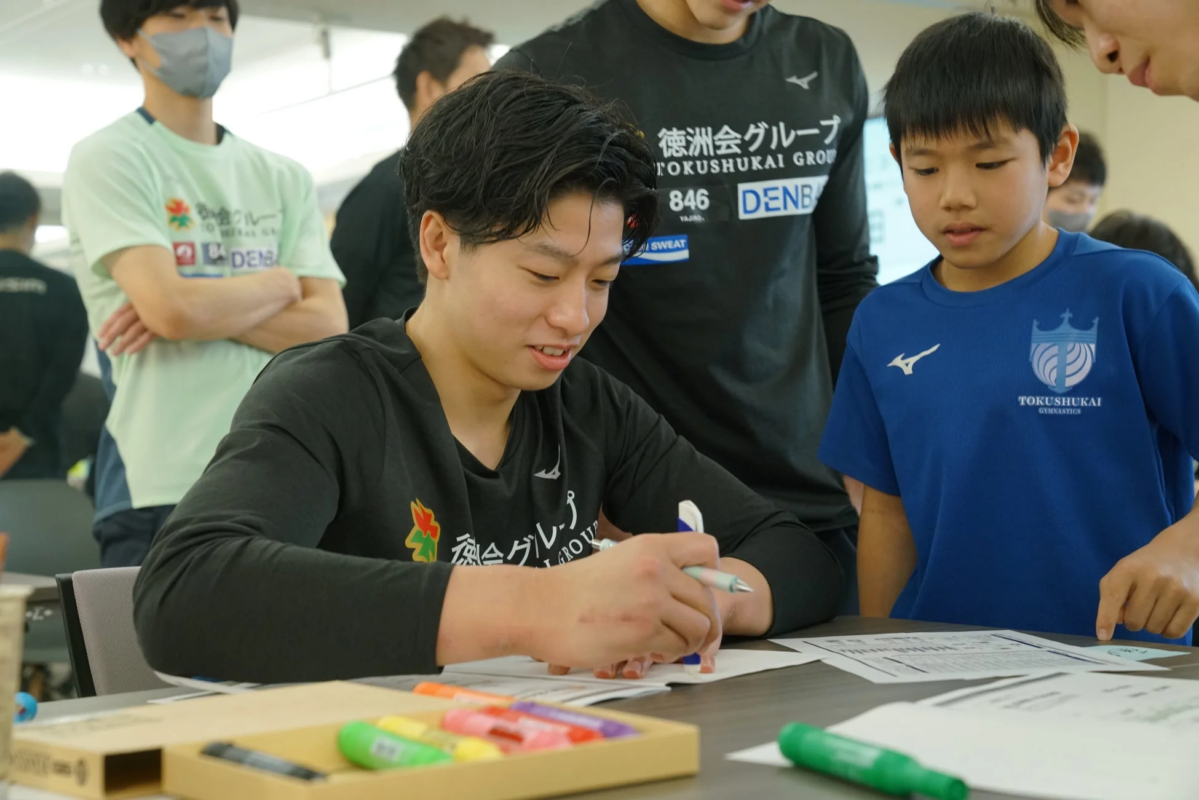 若い男性がテーブルで書類に記入しており、隣の少年が興味深そうに見ている様子