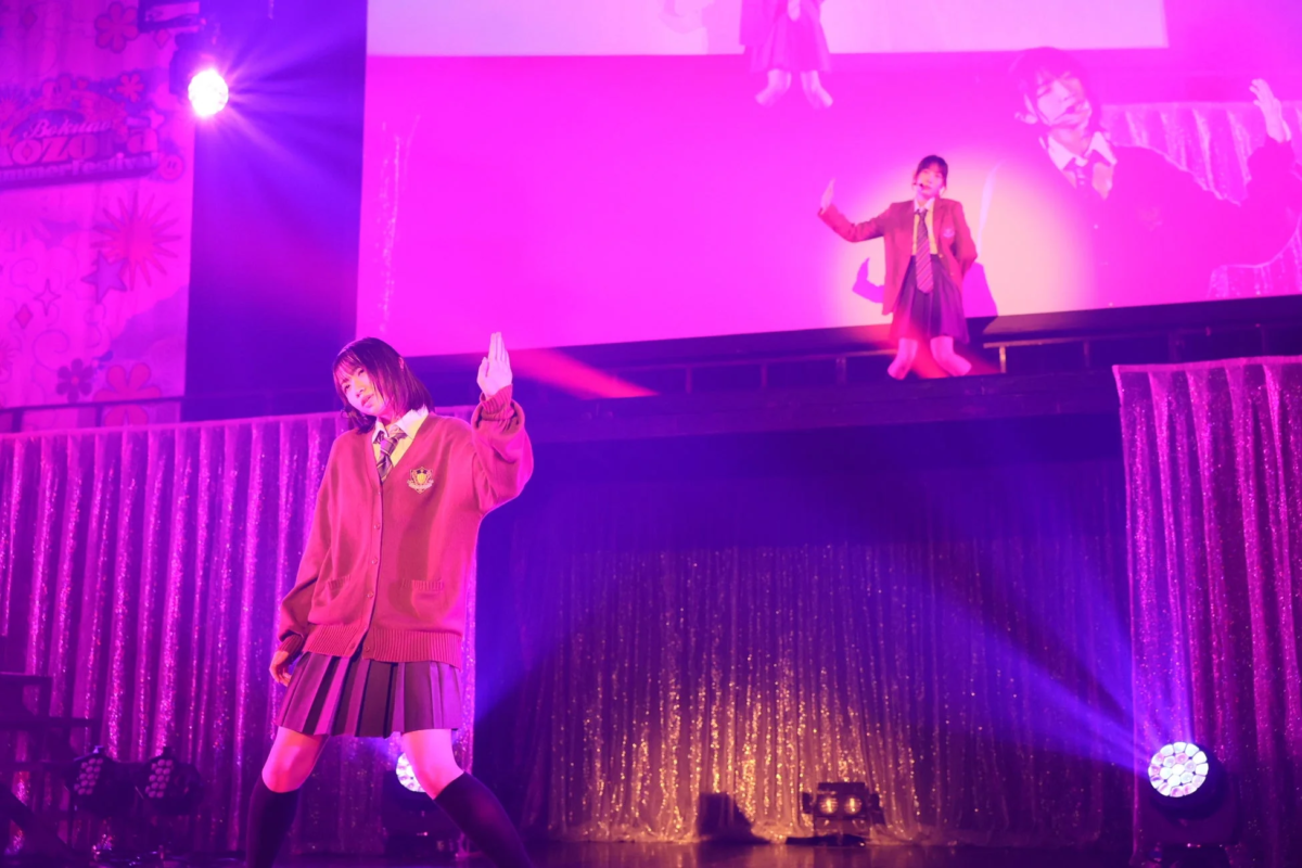 紫とピンクの鮮やかな照明が照らすステージで、制服姿の女性がパフォーマンスしています