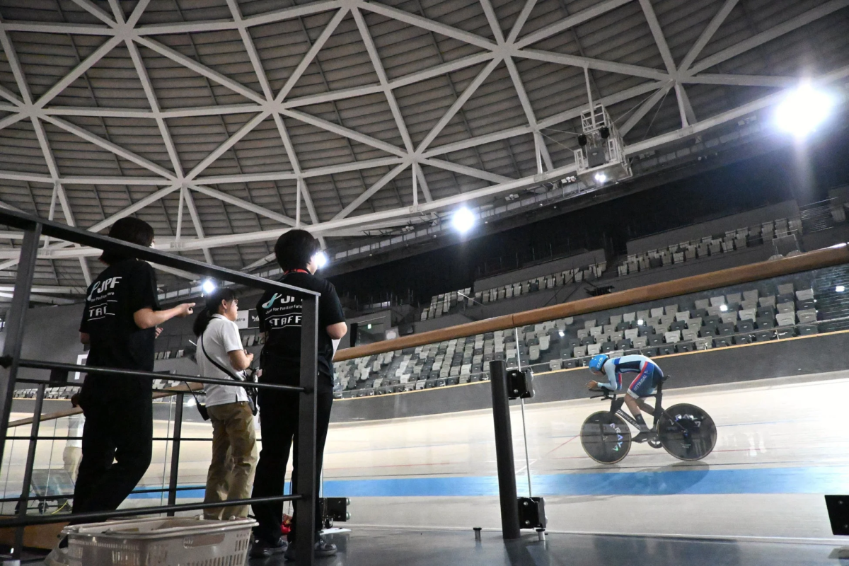 屋内ベロドロームで、スタッフが見守る中、自転車選手がトラックを走行