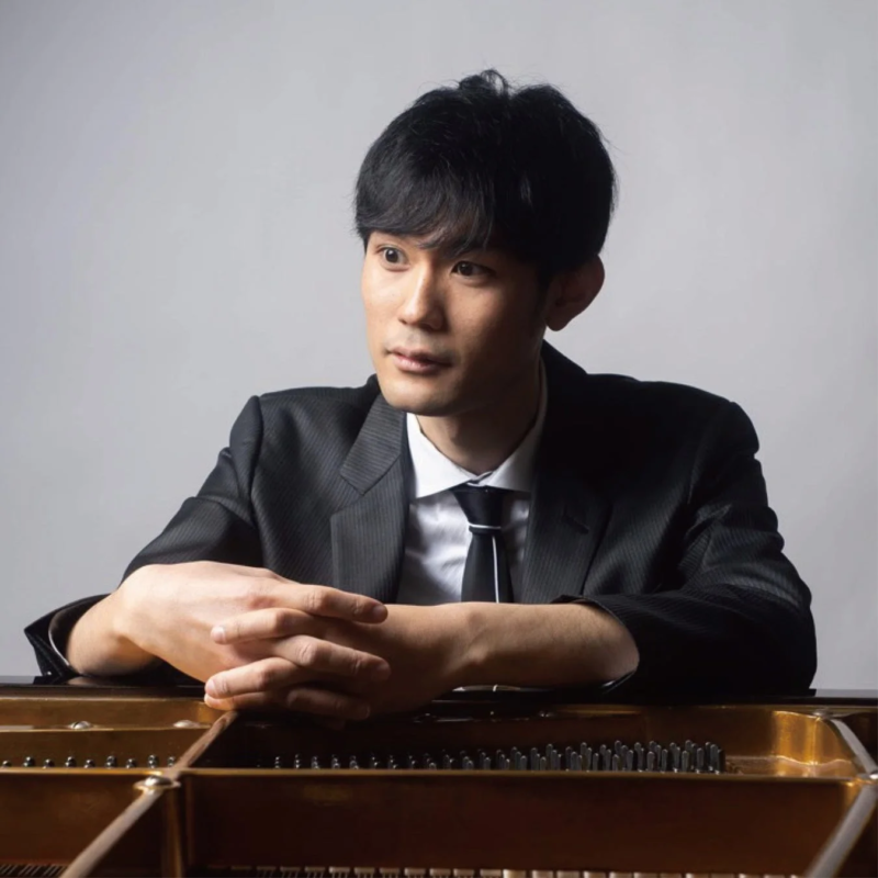 黒いスーツとネクタイを着用した男性がピアノの前に座っているポートレート写真