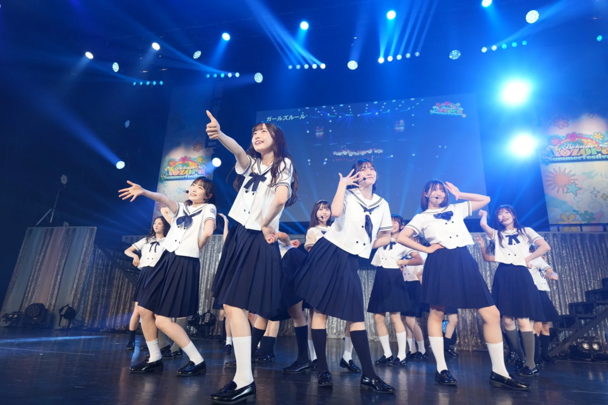 青い照明のステージでセーラー服の女性アイドルグループがパフォーマンス中