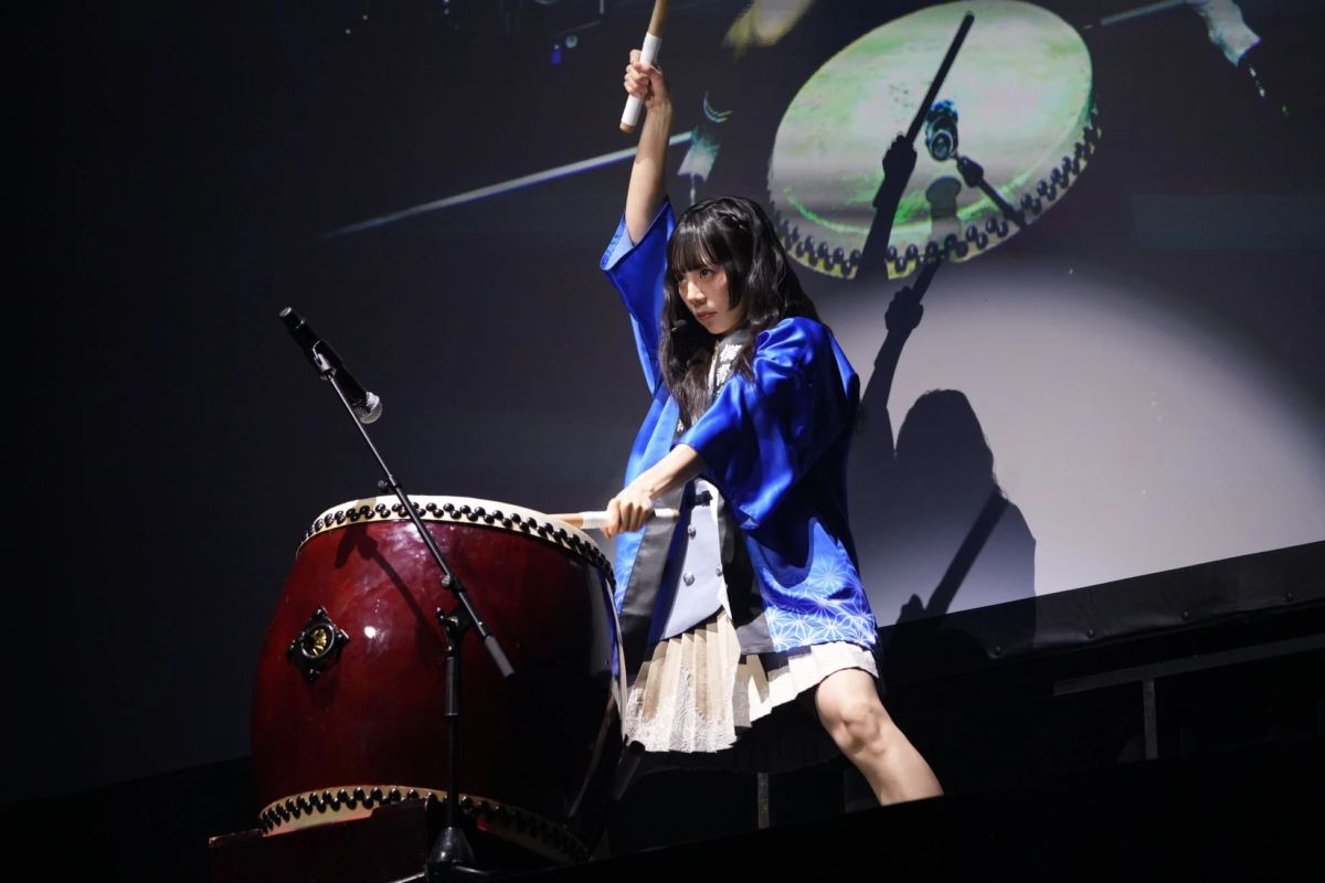青い衣装をまとった女性がステージ上で和太鼓を力強く演奏している様子