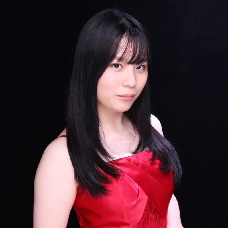 黒い背景の前で、赤いドレスを着用した黒髪の若い日本人女性のポートレートです。彼女はカメラをまっすぐ見つめています。