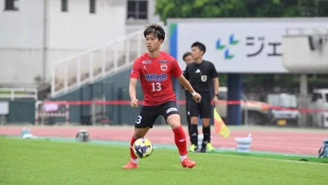 サッカーの試合中、赤いユニフォームと背番号13を着用した選手がボールをドリブルしている瞬間